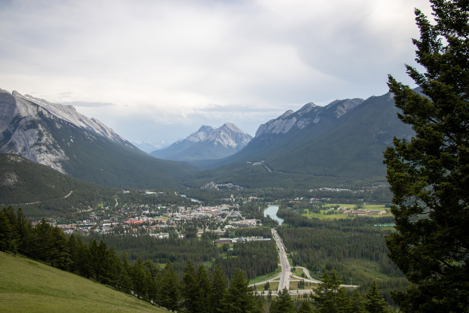 An elevated view over the town of Banff in the Bow Valley, with a highway and river running between forested mountain ridges under cloud.