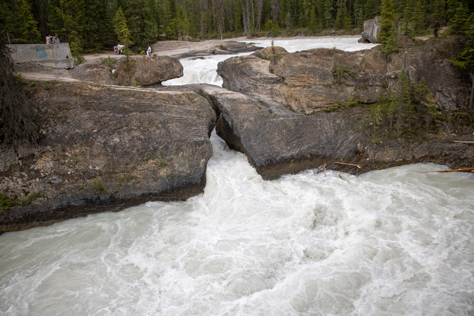 A powerful river forces through a narrow gap beneath a natural rock bridge, throwing up white foam.