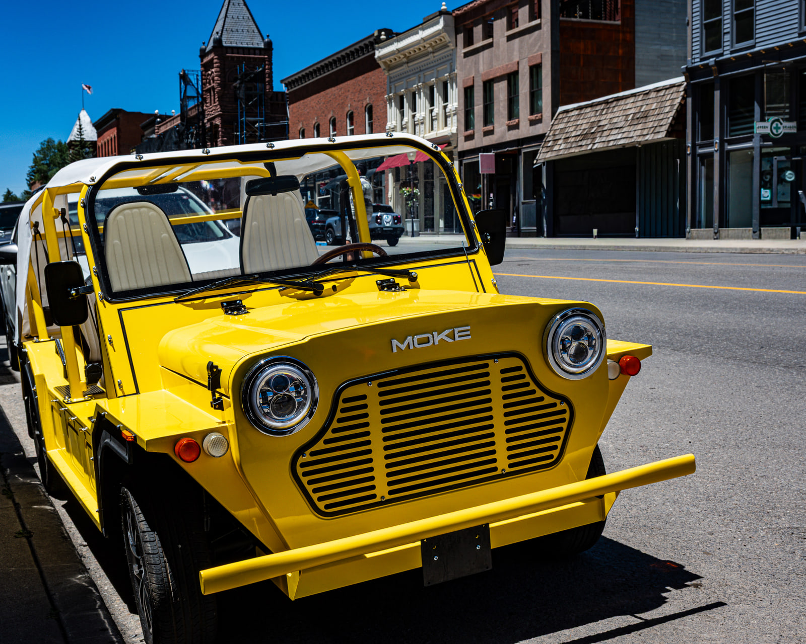 A bright yellow open-sided electric car parked on a historic main street lined with red brick storefronts.
