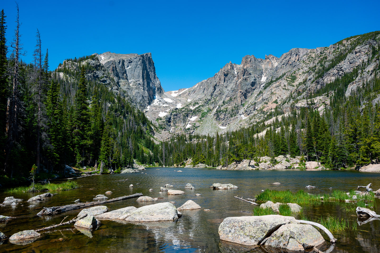 A shallow alpine lake seen across pale granite boulders toward a flat-topped cliff peak under deep blue sky.
