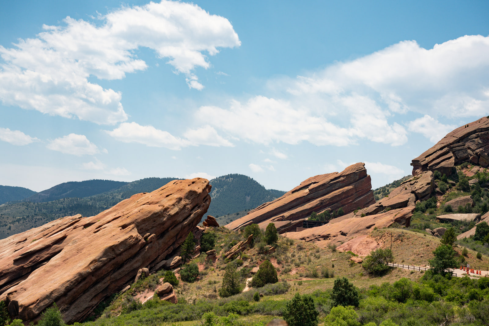 Tilted slabs of red sandstone at Red Rocks Park in Colorado angle across the frame under tall white clouds and blue sky.