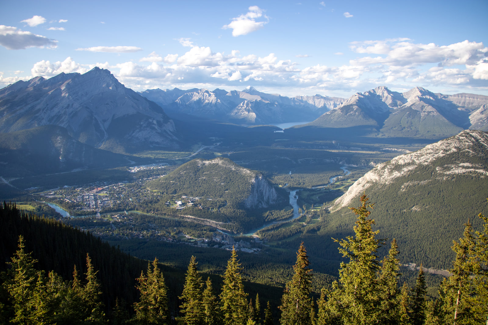 A wide view from a mountain summit over the Bow Valley, showing a small town, a winding river and layers of receding mountain ranges.
