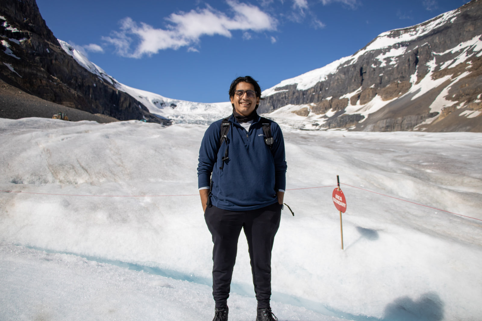 Aditya Shankar standing on the Athabasca Glacier, hands in his pockets, with the icefield headwall and its flanking peaks behind him.